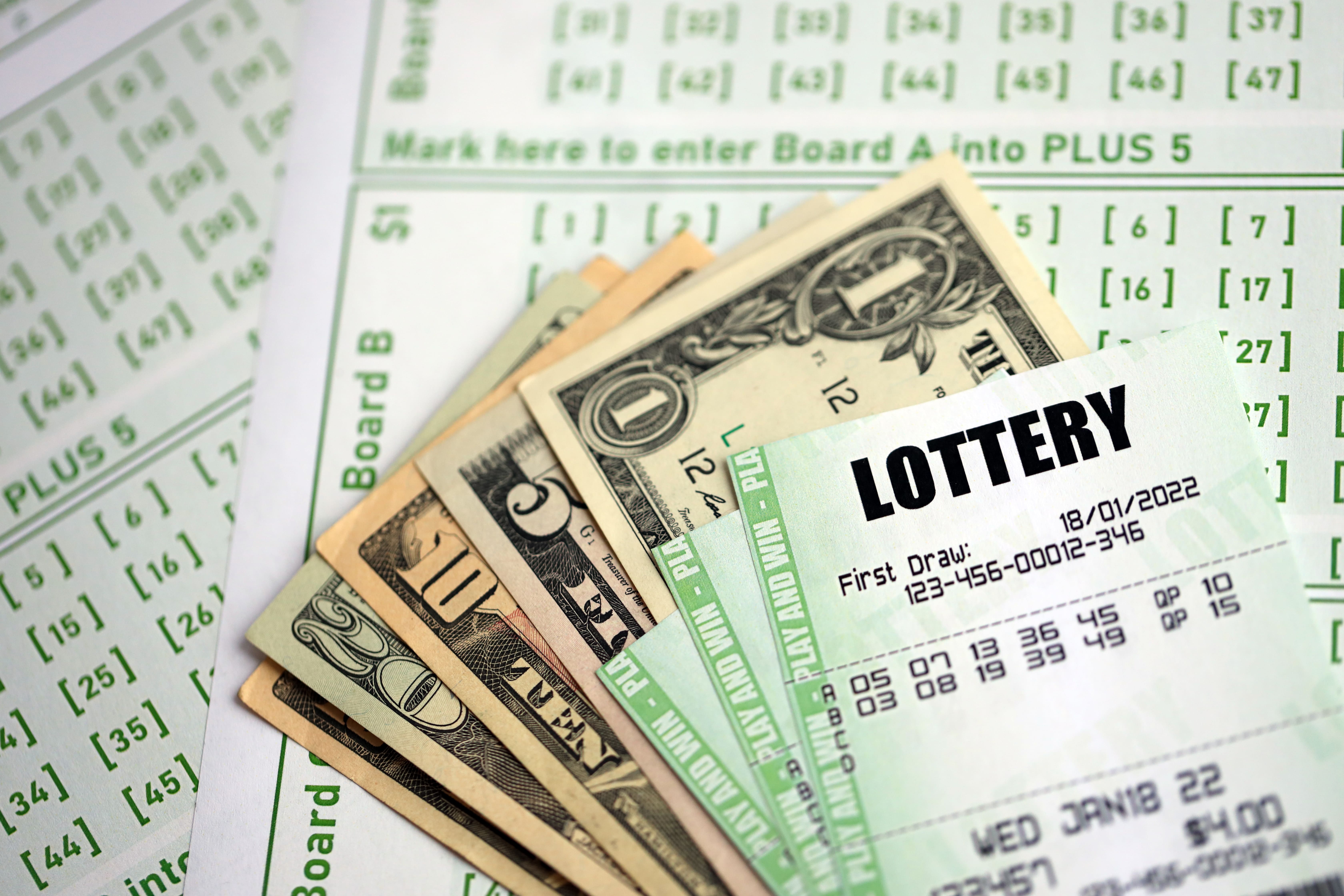 Mano eligiendo números en un boleto de loteria nacional, rodeada de bolígrafos y notas, luz natural y fondo desenfocado.